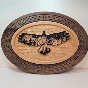 Oval wooden cribbage board with a detailed eagle silhouette in flight, featuring mountains and a night sky within its wings.