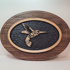 Oval cribbage board with a carved, patterned hummingbird at center, framed by detailed wooden scoring holes.