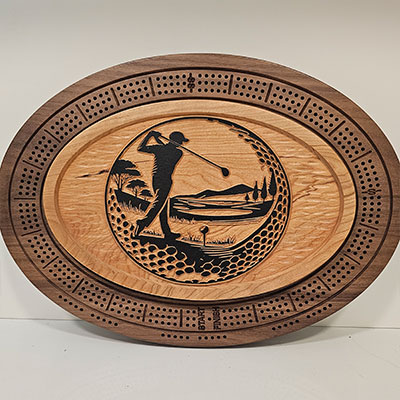 Oval wooden cribbage board with a carved golfer in mid-swing, surrounded by a scenic course and peg holes.