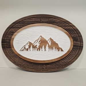 Oval wooden cribbage board featuring mountain and forest scene with natural wood grain background