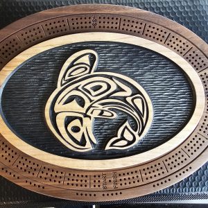 : Oval wooden cribbage board with Indigenous Pacific Northwest Coast tribal eagle design in center