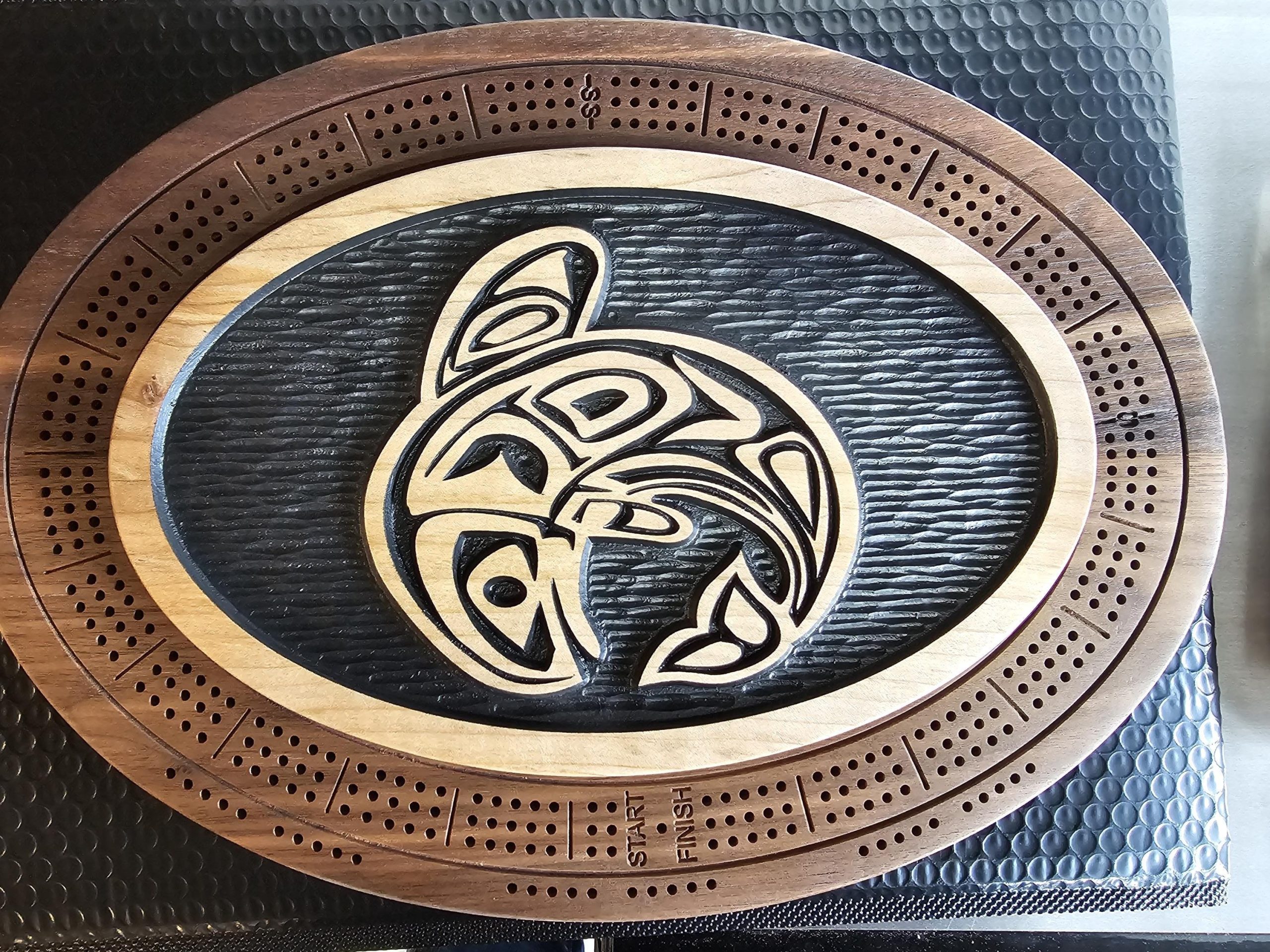 : Oval wooden cribbage board with Indigenous Pacific Northwest Coast tribal eagle design in center