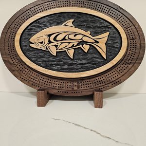 Oval wooden cribbage board with a Native-style salmon design carved in the center, framed by scoring peg holes.